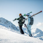 zwei Skifahrer in Skitourenausrüstung mit Rucksack und Ski auf den Schultern