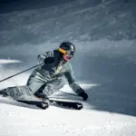 Skifahrer mit Helm und Skibrille carvt in tiefer Schräglage über die frisch präparierte Skipiste